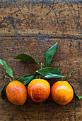 Three blood oranges with leaves in a row on a rustic wooden tabletop