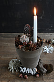 Brennende Kerze in einem Tontopf mit weihnachtlicher Deko