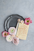 Vintage invitation card and pink flowers on pewter plate