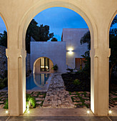View through arch into courtyard with pool at twilight