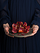 Frau hält Teller mit aufgeschnittenem Granatapfel