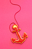 An anchor-shaped biscuit with red icing against a pink background