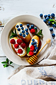White ceramic plate of sweet dessert sandwiches with fresh berries blueberry and raspberry, cream cheese, mint and honey