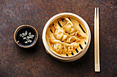 Gyoza dumpling in bamboo steamer, chopsticks and sauce on brown background