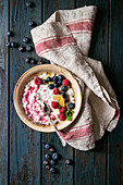 Ceramic bowl of homemade cottage cheese with blueberries, raspberries and honeycombs on kitchen towel over dark wooden plank background