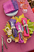 DIY-Serviettenringe aus Birkenast, bunte Servietten und Besteck auf Herbstblatt