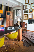 Yellow shell chairs around table with black top and solid wooden legs next to various picture frames on wall