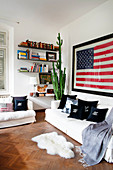 Scatter cushions and blanket on white sofa set, sheepskin rug, wall-mounted shelves, cactus and US flag on wall