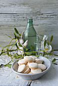 A bowl of anise biscuits with shot glasses, a green bottle and an angel figurine in the background