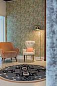 Two retro armchairs on round rug against floral wallpaper