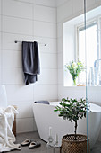 Frei stehende Badewanne im Bad mit weißen Wandfliesen und Fenster