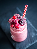 A frozen smoothie with berries in a glass with a straw (vegan)