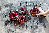 Hand greift nach Donuts mit Blaubeerglasur und Glitzerpulver