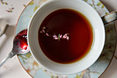 Eine Tasse schwarzer Tee mit Kräutern und Löffel mit roter Marmelade