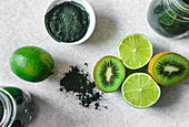 Halved kiwi and lime fruits, powdered spirulina, green smoothie in glass jars