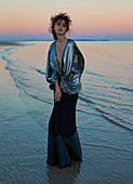 Dunkelhaarige Frau in langem, Abendkleid bei Sonnenuntergang am Meer