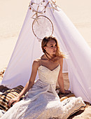 A young woman in a tepee in the desert wearing a long white dress