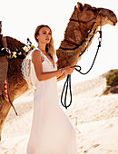 A young woman wearing a long white wedding dress with a camel