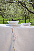 DIY-Tischdecke und Frühstücksgeschirr mit Kirschblütenmotiv auf Tisch unter blühendem Kirschbaum im Garten
