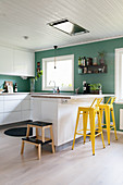 Petrol-blue walls and yellow bar stools in modern kitchen