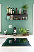Black shelf mounted on petrol-blue kitchen wall above hob