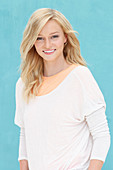 A young blonde woman wearing a white jumper and an apricot t-shirt against a blue background