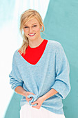 A young blonde woman wearing a red, top and a blue jumper