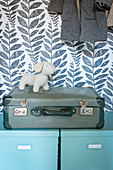 Hellblaue Aufbewahrungsboxen, Koffer und Hundefigur im Schrank vor Tapete