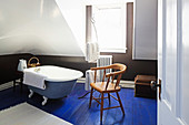 Old chair next to free-standing bathtub on blue-painted wooden floor