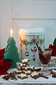 Glühwein, Zimtsterne, Weihnachtsstern, tannenbaumförmige Kerze und Blechdose