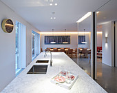Island counter with marble top and mirrored wall in elegant kitchen with dining area in background