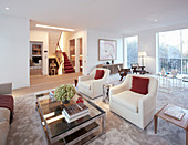 White armchairs and glass-topped coffee table in foreground in front of set of tables and wooden armchairs next to terrace windows