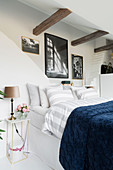 Double bed below rustic wooden beams in white bedroom