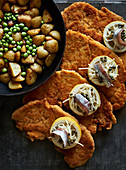 Breaded ham escalopes with lemon, anchovies and capers served with fried potatoes and peas