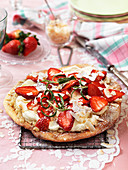 Sweet pizza with almond cream, whipped cream, strawberries and rosemary