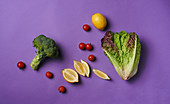 Cos lettuce, broccoli, cherry tomatoes and lemons on a purple surface