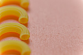 Elbow macaroni in a row on a coloured surface (close-up)