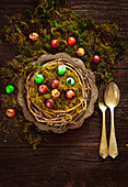 Dyed Easter eggs in an Easter nest made from twigs and moss on a wooden table (seen from above)