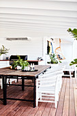 Dining table with rustic wooden top and white rattan chairs on veranda