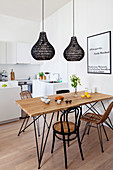 Dining table and various chairs below black pendant lamps in open-plan kitchen