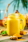 Yellow fruit smoothie with turmeric and ingredients on a table