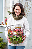 Woman bringing wire basket with Christmas baubles, cones and moss