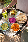 A woman serving a tray of salad, dips and flatbread in the garden