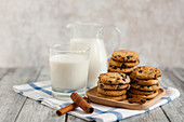 Milk in a jar and a jug, with chocolate chip cookies and cinnamon sticks