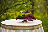 Purple lilac on cake stand on table with ornate tablecloth in garden