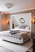 Double bed with head in niche in bedroom with patterned wallpaper