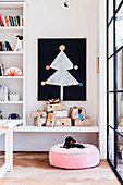 Stiliesierter Weihnachtsbaum aus Papier auf schwarzer Wandtafel, darunter Geschenk auf Ablage und Kissen mit Hund