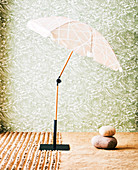 Parasol with umbrella stand and natural stones in front of wallpapered wall