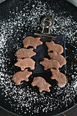 Pig-shaped gluten-free biscuits on a black plate surrounded by a dusting of icing sugar