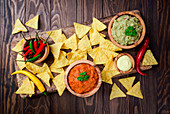 Mexican nachos with guacamole, salsa and cheese dip in wooden bowls on dark background